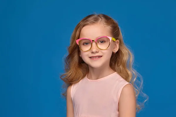 Divatos kislány rózsaszín ruha és a szemüveg, olyan édesség a kezében, állandó kék háttérrel. — Stock Fotó