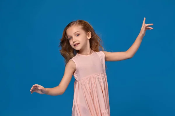 Petite fille à la mode dans une robe rose pose sur un fond bleu . — Photo