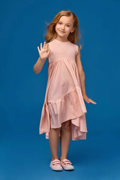 Niña de moda en un vestido rosa está posando sobre un fondo azul . —  Fotos de Stock