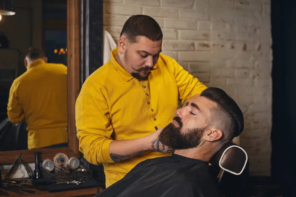 Client with big black beard during beard shaving in barber shop