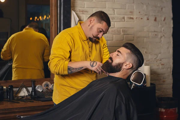 Client with big black beard during beard shaving in barber shop
