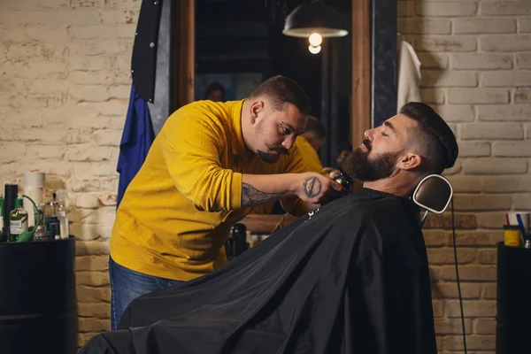 Client with big black beard during beard shaving in barber shop