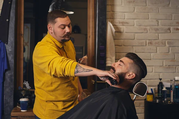 Client with big black beard during beard shaving in barber shop