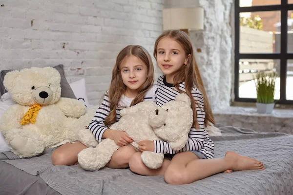Изображение двух маленьких сестер, сидящих на кровати в комнате . — стоковое фото