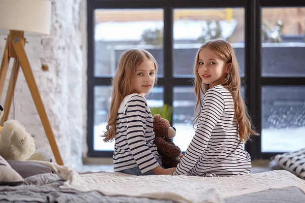 A imagem de duas irmãzinhas sentadas na cama no quarto . — Fotografia de Stock