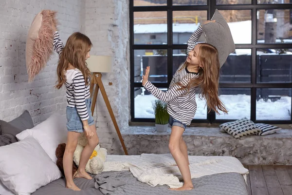 L'image de deux petites sœurs assises sur le lit dans la chambre. Ils utilisent un oreiller pour se battre. — Photo