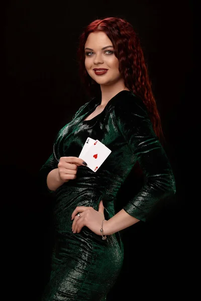 Giovane donna dai capelli rossi in posa con una carta da gioco in mano, su sfondo nero — Foto Stock