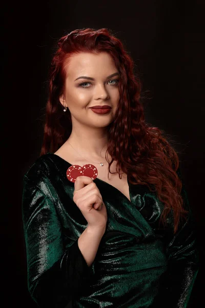 Sexy redheaded woman whith a curly hair posing with chips in her hands, on black background