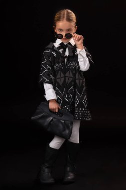 Küçük kız siyah gözlük, karanlık panço, siyah çizmeler ve onun elinde bir debriyaj