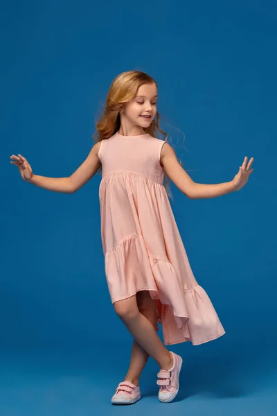 Niña de moda en un vestido rosa está posando sobre un fondo azul . — Foto de Stock