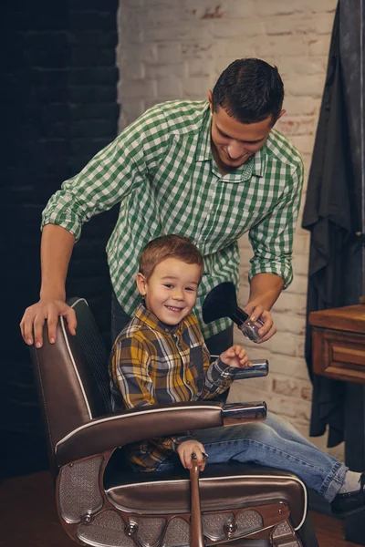 Elegantní malé dítě sedí na židli v holičství se svým mladým otcem na pozadí — Stock fotografie