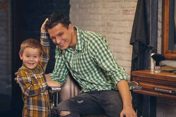 Jovem pai bonito e seu pequeno filho elegante na barbearia à espera de barbeiro — Fotografia de Stock