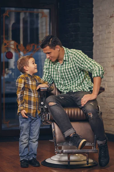 Jovem pai bonito e seu pequeno filho elegante na barbearia à espera de barbeiro — Fotografia de Stock