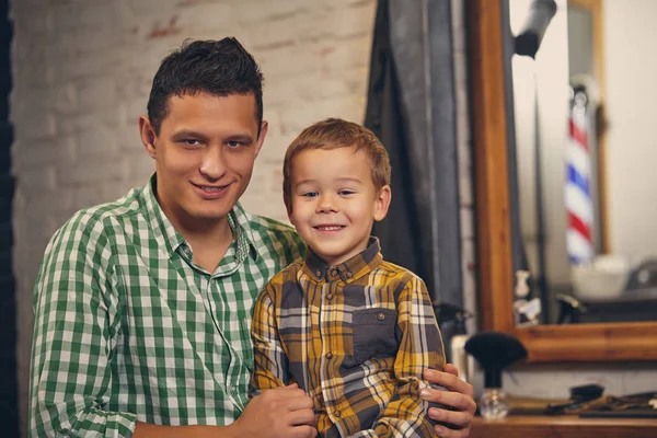 Mladý pohledný otec a jeho malý stylový syn v holičství čeká na holiče — Stock fotografie
