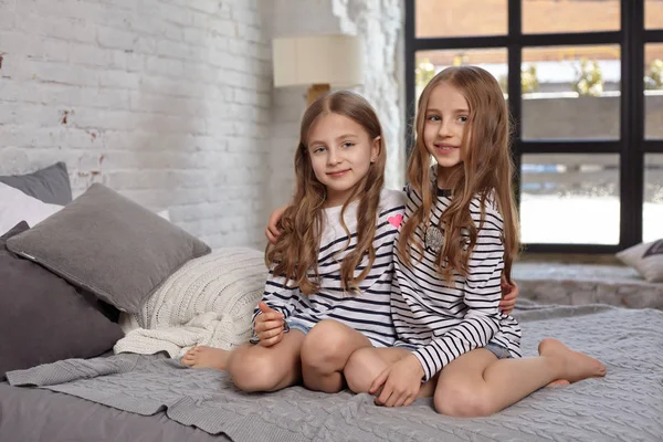 Изображение двух маленьких сестер, сидящих на кровати в комнате . — стоковое фото