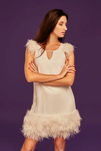 Красива брюнетка в елегантній коктейльній білій сукні позує в студії на фіолетовому фоні . — стокове фото