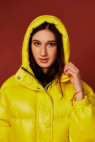 Porträtt av brunett ung kvinna som bär överdimensionerade gul dunjacka med huva. Studio nära upp skott. — Stockfoto
