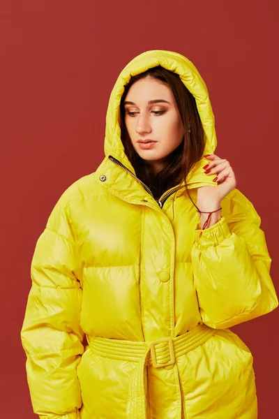 Retrato de una joven morena vestida con una sobredimensionada chaqueta amarilla con capucha puesta. Estudio primer plano plano . — Foto de Stock