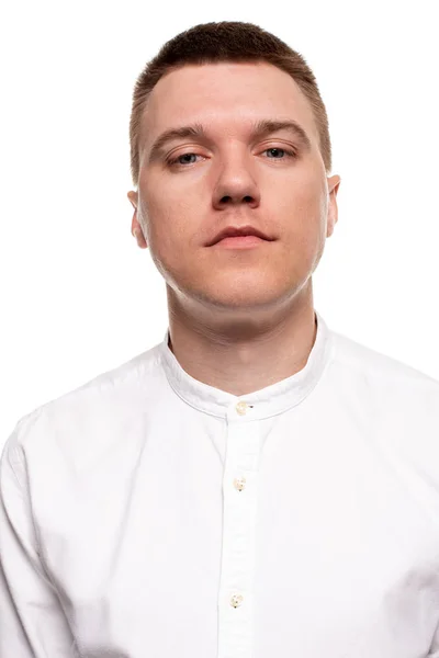 Jovem bonito encantador em uma camisa branca está fazendo rostos, enquanto está isolado em um fundo branco — Fotografia de Stock
