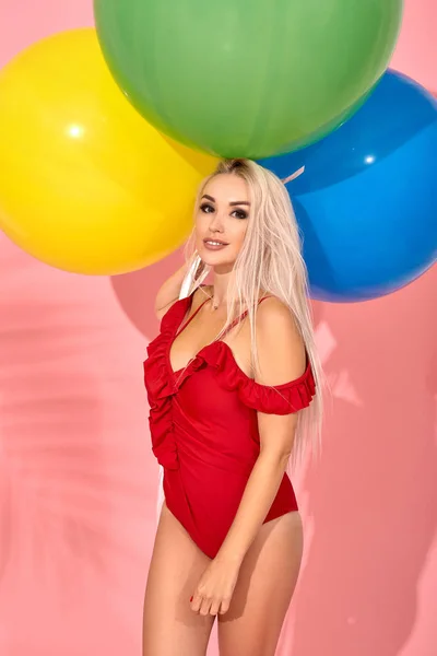 Jonge sexy slanke vrouw in een rode zwembroek met ballonnen in haar hand is poseren in een studio. — Stockfoto