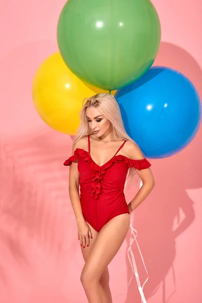 Jonge sexy slanke vrouw in een rode zwembroek met ballonnen in haar hand is poseren in een studio. — Stockfoto