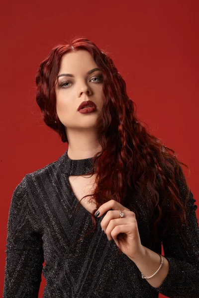 Bella donna sexy è in posa in un abito a maglia su uno sfondo rosso. Trucco serale. Capelli ricci lunghi, sani, rossi . — Foto Stock