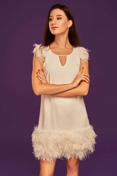 Красива брюнетка в елегантній коктейльній білій сукні позує в студії на фіолетовому фоні . — стокове фото