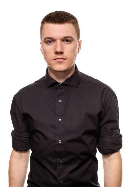 Guapo joven con una camisa negra está haciendo caras, mientras está de pie aislado sobre un fondo blanco — Foto de Stock