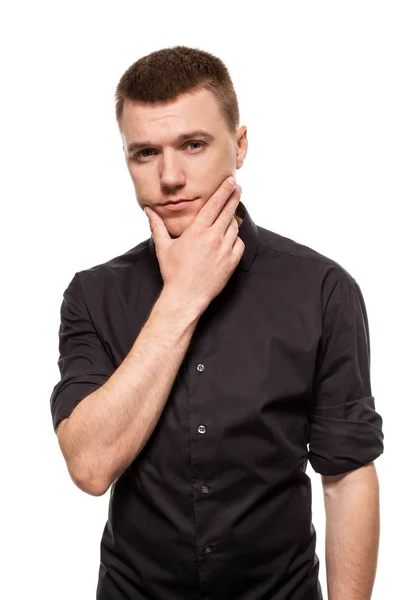 Красивый молодой человек в черной рубашке корчит рожи, стоя изолированным на белом фоне — стоковое фото