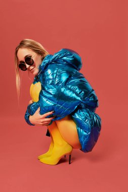 Genç sevimli güzel sarışın kız mavi ceketli bir cenin pozisyonu Studio kamera, kırmızı arka plan önce oturuyor. Yan görünüm