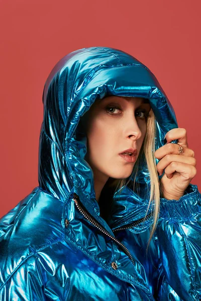 Блондинка струнка дівчина в синій куртці покриває обличчя від вітру з капюшоном — стокове фото