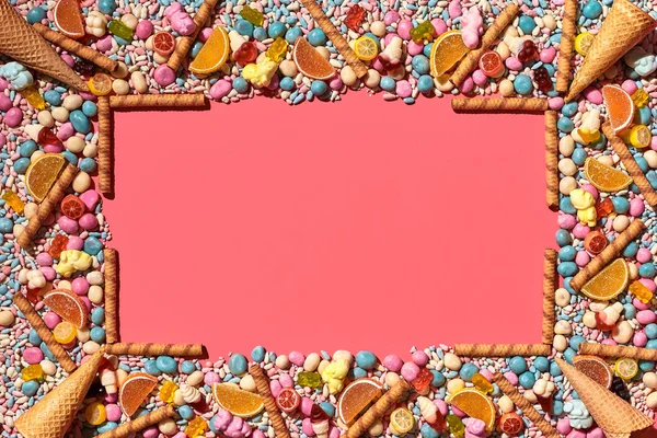 Multicolored glazed dragees and other sweets are arranged in the form of a frame on a coral background. — Stock Photo, Image