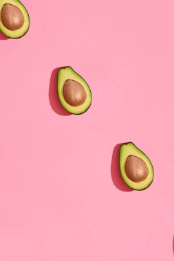 Renkli meyve desen mercan pembe arka plan, üstten görünüm üzerinde çukurları ile taze kesilerek avokado yarıya indirir