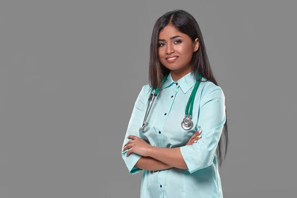 Αξιολάτρευτο ινδική γυναίκα γιατρός νοσοκόμα με στηθοσκόπιο στο γαλαζοπράσινο φόρεμα σε γκρι φόντο — Φωτογραφία Αρχείου