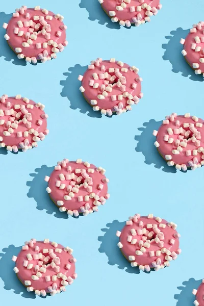 Food design with tasty pink glazed donut on blue pastel background top view pattern