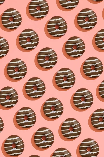 Food design with tasty chocolate glazed donut with white strips on coral peach pastel background top view pattern