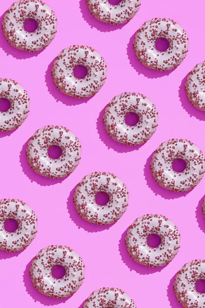 Food design with tasty pink glazed donut on purple lilac pastel background top view pattern
