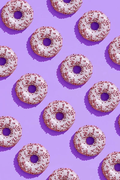 Diseño de alimentos con sabroso rosado esmaltado donut en lila púrpura pastel fondo superior ver patrón — Foto de Stock