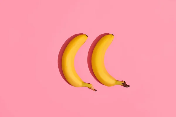 Komposition eines Bananenpaares, das neben einem rosa Hintergrund in der Bildmitte liegt, Ansicht von oben — Stockfoto