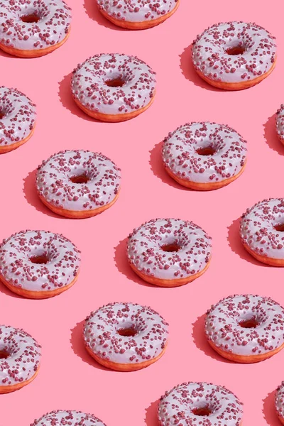 Food design with tasty pink glazed donut on coral pink pastel background top view pattern