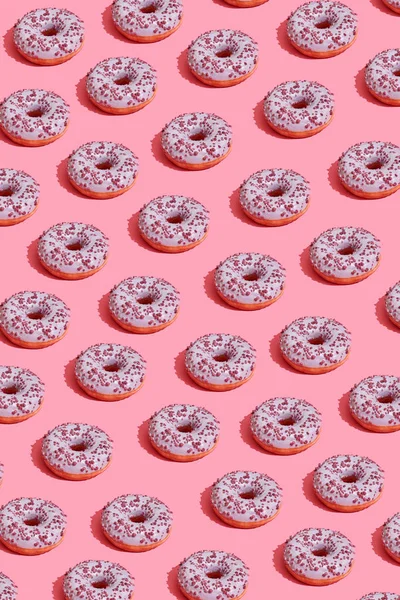 Food design with tasty pink glazed donut on coral pink pastel background top view pattern