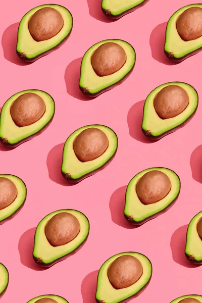 Färgglada frukt mönster av färska kapade avocado halvor med gropar på korall rosa bakgrund, ovanifrån — Stockfoto