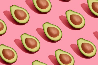 Renkli meyve desen mercan pembe arka plan, üstten görünüm üzerinde çukurları ile taze kesilerek avokado yarıya indirir