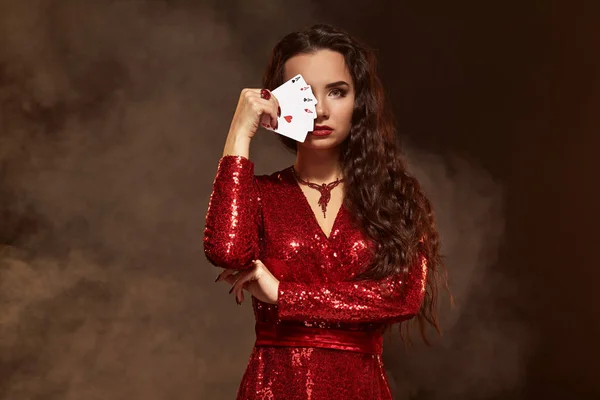 赤いイブニング ドレスの若い美しい幸運なブルネットが表示されます彼女のカードは、エースの 4 カードで顔を隠して — ストック写真