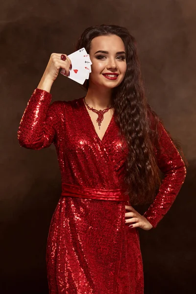 Mladá krásná štěstí brunetka v červené večerní šaty ukazuje její karet, čtyři esa, drží karty v blízkosti její tvář — Stock fotografie