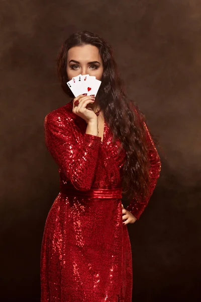 Junge schöne glückliche Brünette in einem roten Abendkleid zeigt ihre Karten, eine Vier aus Assen, versteckt ihr Gesicht mit Karten — Stockfoto