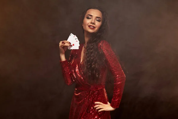 Giovane bella bruna fortunata in un abito da sera rosso mostra le sue carte, un quattro di assi — Foto Stock