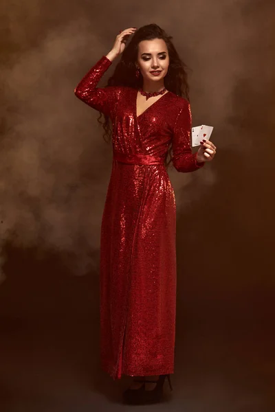 Joven morena hermosa suerte en un vestido de noche rojo muestra sus tarjetas, un par de ases — Foto de Stock