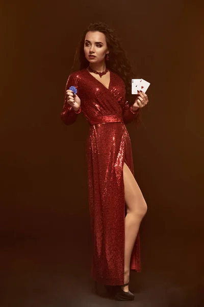 Joven mujer morena hermosa suerte en un vestido de noche rojo, coquetea, muestra sus cartas en una mano y fichas en otra mano . — Foto de Stock