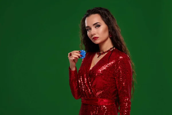 Νέοι αρκετά τυχερός μελαχρινή γυναίκα σε ένα κόκκινο φόρεμα βράδυ κατέχει μερικές πόκερ μάρκες στα χέρια της σε πράσινο φόντο — Φωτογραφία Αρχείου